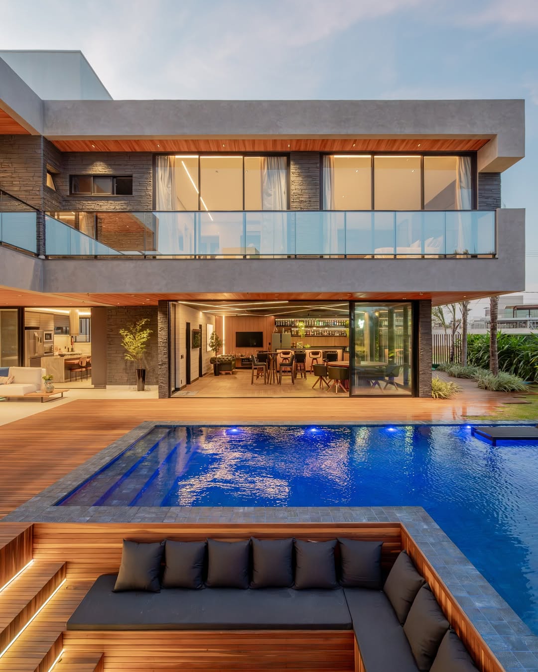 Fachada contemporânea iluminada com piscina e deck de madeira